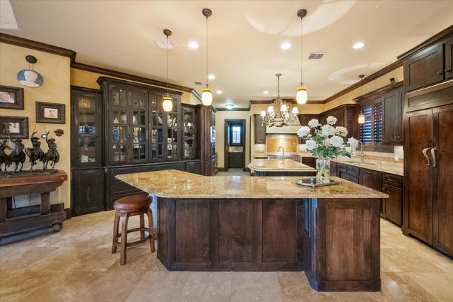 Kitchen featuring a large island, crown molding, knotty alder cabinetry, and glass insert cabinets | Image 10