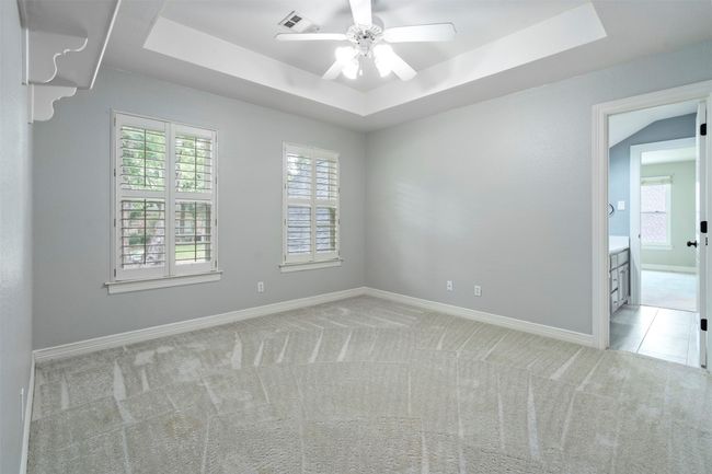 Empty room with light colored carpet, a raised ceiling, a ceiling fan, and baseboards | Image 22