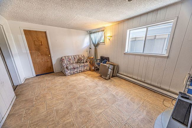 Living area featuring a baseboard radiator, tile patterned flooring, wooden walls, and a textured ceiling | Image 48