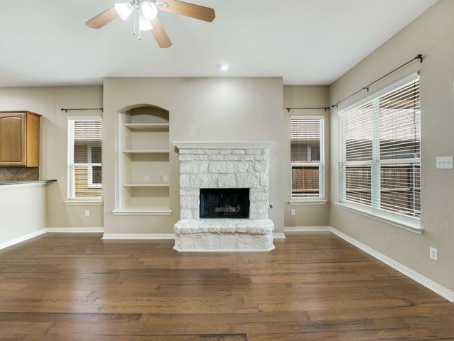 Unfurnished living room featuring dark wood finished floors, a ceiling fan, a fireplace, and built in shelves | Image 10