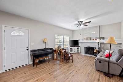 Living room featuring ceiling fan, light hardwood / wood-style flooring, a textured ceiling, and a fireplace | Image 3