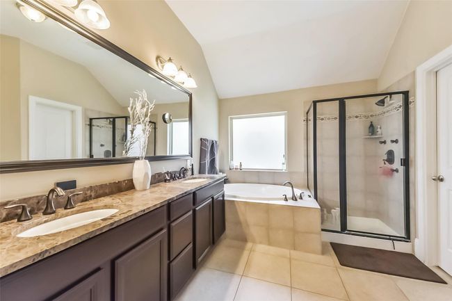 The spacious primary en-suite features a double vanity with a marble countertop, a large mirror, and elegant lighting. It includes a soaking tub and a glass-enclosed shower, providing a luxurious and functional space. | Image 20