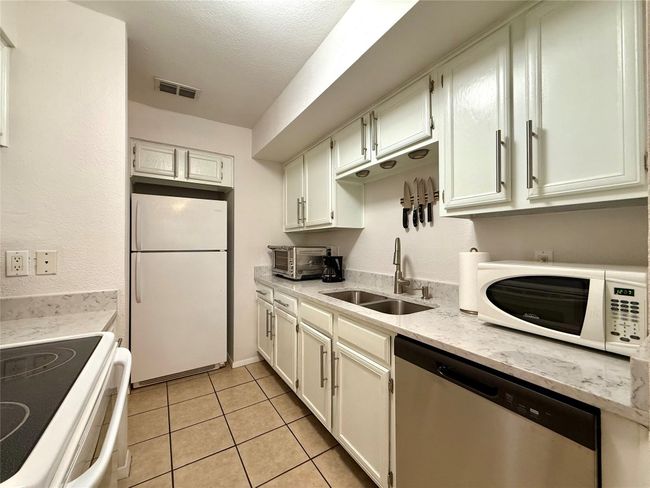 Kitchen with white appliances, light tile patterned floors, a sink, visible vents, and a textured ceiling | Image 5