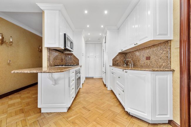 Kitchen with stainless steel appliances, white cabinetry, light stone countertops, recessed lighting, and crown molding | Image 9