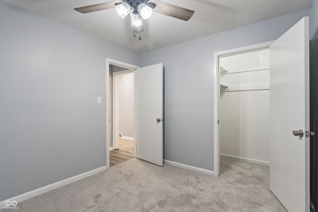 unfurnished bedroom with carpet flooring, baseboards, a closet, ceiling fan, and a walk in closet | Image 23