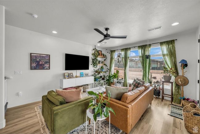 Living area with a textured ceiling, light wood-style flooring, baseboards, visible vents, and ceiling fan | Image 7
