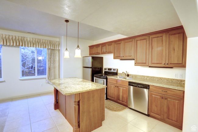 Kitchen featuring a center island, decorative light fixtures, a sink, stainless steel appliances, and light stone counters | Image 37