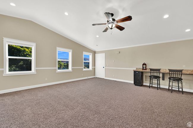 Carpeted empty room featuring built in desk, lofted ceiling, and ceiling fan | Image 46