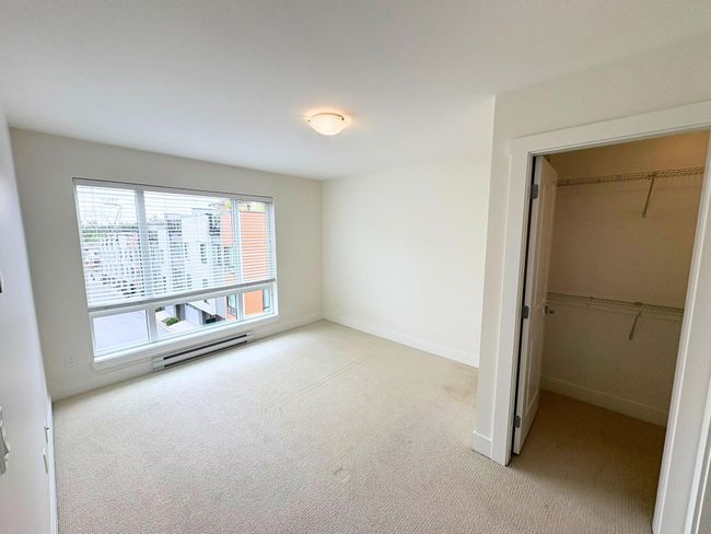 Unfurnished bedroom with light carpet, a walk in closet, a closet, and a baseboard heating unit | Image 7