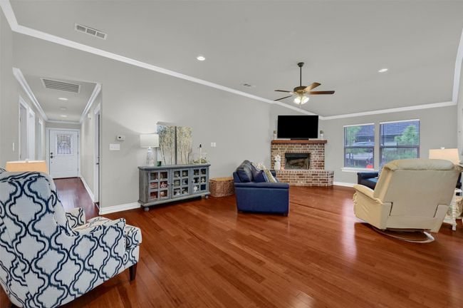 Living room featuring ornamental molding, ceiling fan, visible vents, a fireplace, and wood finished floors | Image 7