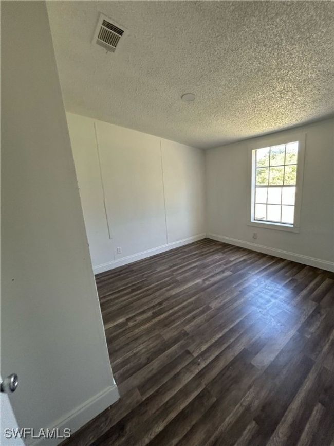 Empty room featuring a textured ceiling, baseboards, visible vents, and dark wood finished floors | Image 6