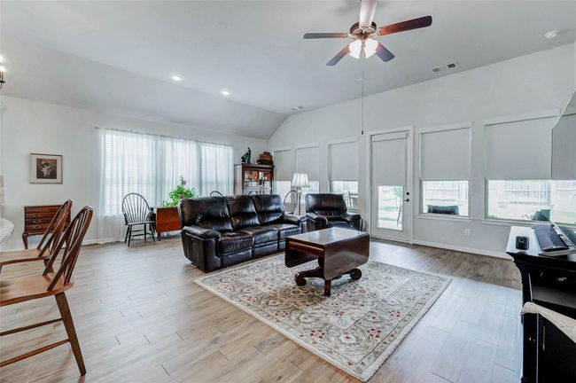 The family room offers soaring ceilings and stylish wood-look tile flooring, creating a warm and inviting space. A ceiling fan adds both comfort and charm, while a wall of windows fills the room with natural light and provides a lovely view of the backyard. | Image 9