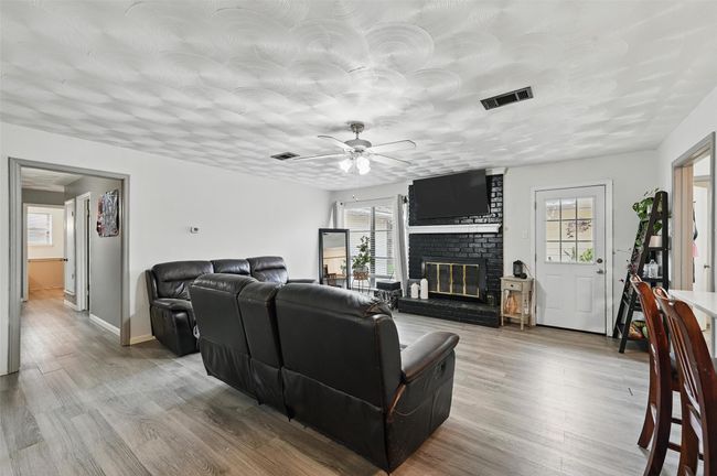 Living room featuring a brick fireplace, ceiling fan, light wood-type flooring, and baseboards | Image 7