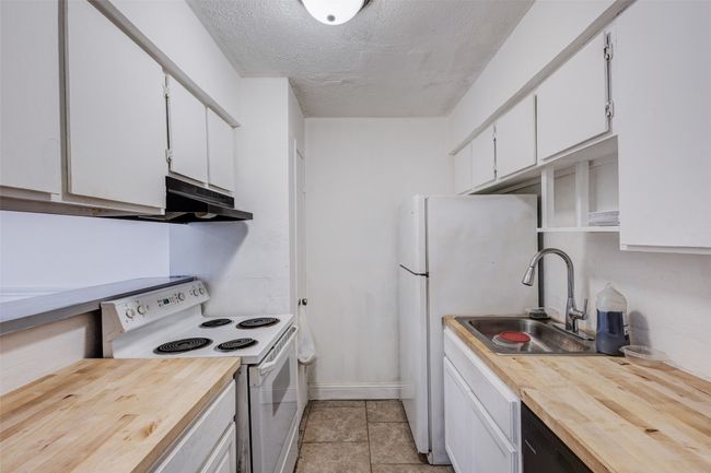 Kitchen with wooden counters, under cabinet range hood, white appliances, white cabinetry, and a sink | Image 7