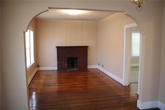 Unfurnished living room featuring arched walkways, a fireplace, wood finished floors, visible vents, and baseboards | Image 4
