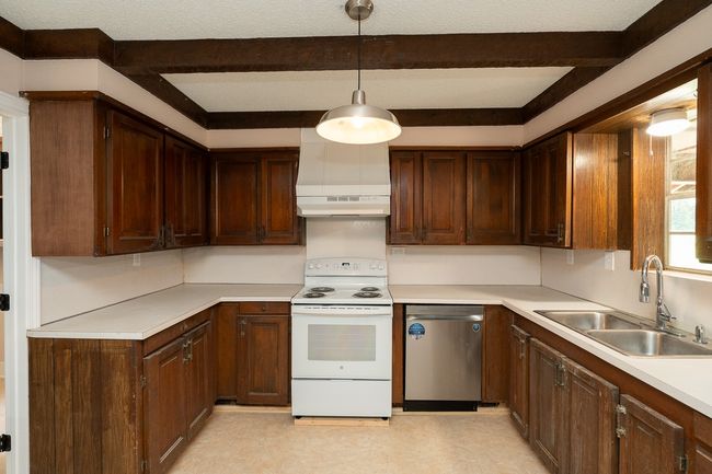 Kitchen featuring white electric stove, stainless steel dishwasher, beamed ceiling, light countertops, and under cabinet range hood | Image 14