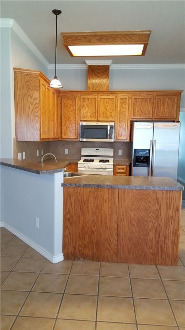 Kitchen featuring stainless steel appliances, a peninsula, tasteful backsplash, light tile patterned floors, and pendant lighting | Image 10
