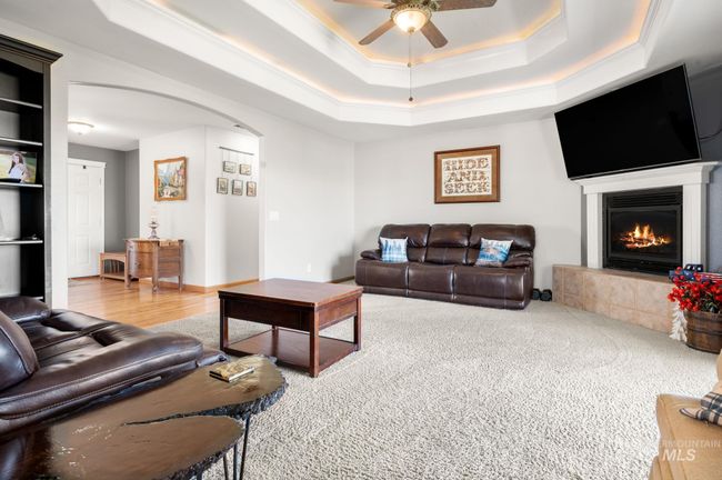 Living room with arched walkways, ceiling fan, a fireplace, crown molding, and a double tray ceiling | Image 17