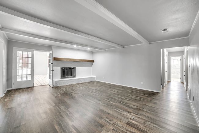 Unfurnished living room featuring dark wood finished floors, a brick fireplace, beamed ceiling, and visible vents | Image 23
