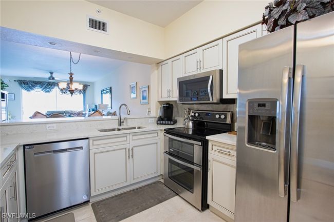 Kitchen featuring white cabinetry, light stone countertops, stainless steel appliances, sink, and light tile floors | Image 9