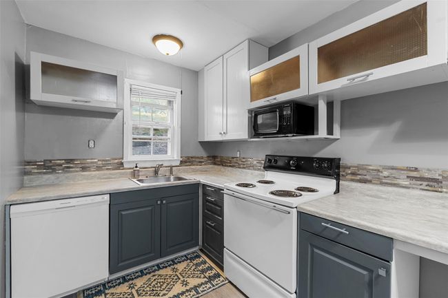 Kitchen with white appliances, glass insert cabinets, light countertops, and a sink | Image 8