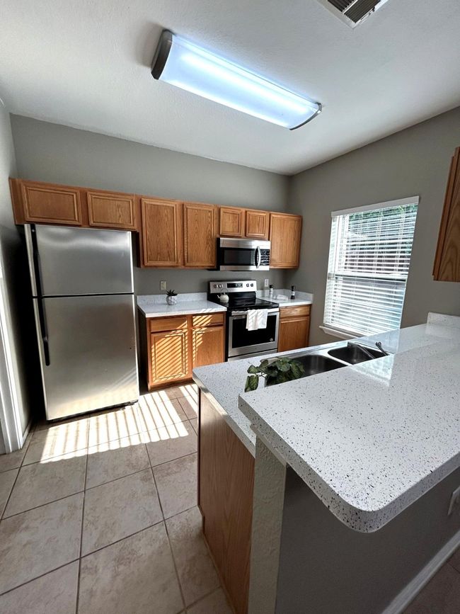 Kitchen with appliances with stainless steel finishes, brown cabinetry, light countertops, light tile patterned floors, and a peninsula | Image 5