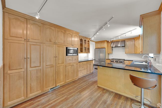Kitchen featuring stainless steel appliances, wall chimney range hood, rail lighting, a sink, and light brown cabinets | Image 8