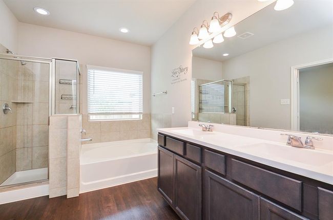 The appealing dark/light theme continues in the primary ensuite bath, with dual sinks, tons of storage below; a wall-wide mirror and delicate lighting above.. The walk-in shower and garden tub sit side-by-side. | Image 14