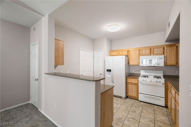 Kitchen with visible vents, dark countertops, white appliances, and a peninsula | Image 15