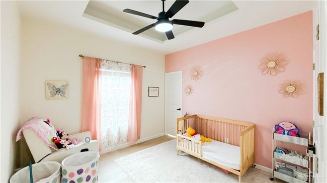 Bedroom featuring a nursery area, a raised ceiling, ceiling fan, and wood finished floors | Image 5