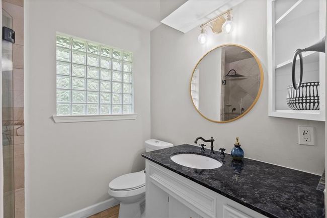 Elegant ensuite bath in additional bedroom with black granite countertop, gold mirror, standing shower and glass block window for natural light. | Image 35