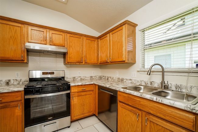 Kitchen with stainless steel range with gas cooktop, dishwashing machine, under cabinet range hood, vaulted ceiling, and light countertops | Image 10