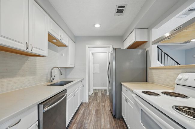 Kitchen with stainless steel appliances, white cabinetry, decorative backsplash, wall chimney range hood, and dark wood-type flooring | Image 7