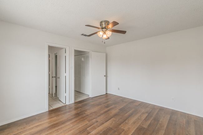 Unfurnished bedroom featuring wood finished floors, a textured ceiling, ensuite bath, baseboards, and ceiling fan | Image 16