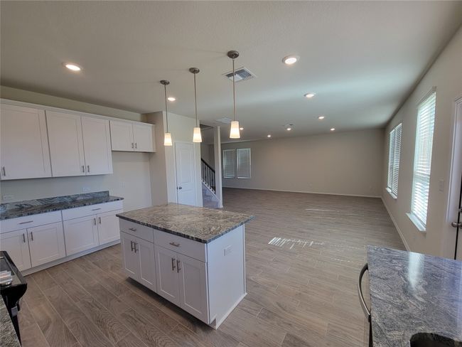 Kitchen with white cabinets, visible vents, dark stone counters, decorative light fixtures, and light wood-type flooring | Image 5