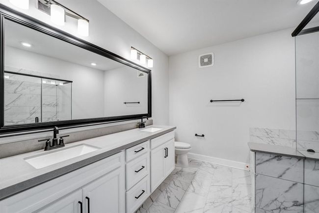 This bathroom features a spacious double vanity with modern fixtures, a large mirror, and sleek cabinetry. The room is accented with elegant marble tile flooring and a glass-enclosed shower, creating a clean and sophisticated look. | Image 15
