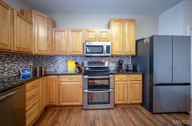 Kitchen with stainless steel appliances, dark wood-style flooring, tasteful backsplash, and dark stone counters | Image 10