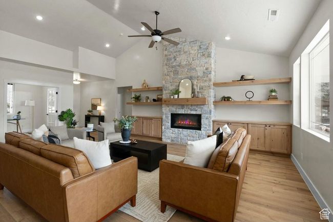 Living area featuring high vaulted ceiling, ceiling fan, light wood finished floors, a fireplace, and visible vents | Image 7