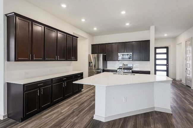 Living room is open to the kitchen featuring stainless steel appliances, light countertops, dark wood-style floors, a breakfast with sink and recessed lighting | Image 7