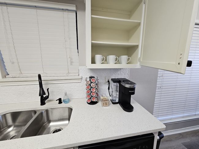 Kitchen with a sink, backsplash, dishwashing machine, light stone countertops, and white cabinetry | Image 15