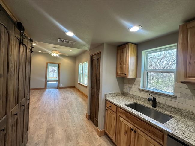 Kitchen featuring a textured ceiling, visible vents, light wood finished floors, a sink, and backsplash | Image 20
