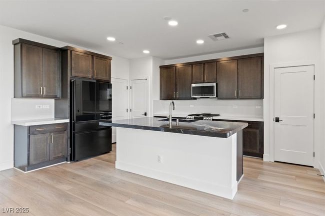 Kitchen with stainless steel microwave, freestanding refrigerator, dark brown cabinets, a sink, and visible vents | Image 8