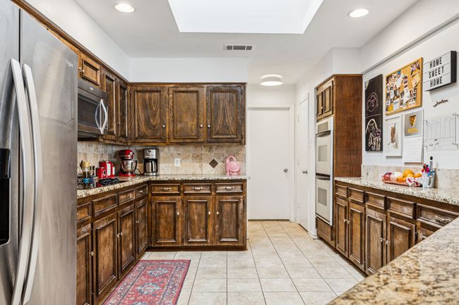 Kitchen with appliances with stainless steel finishes, decorative backsplash, light tile patterned flooring, light stone countertops, and dark brown cabinets | Image 9