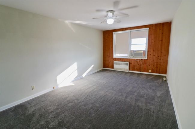 Unfurnished room with radiator, dark carpet, ceiling fan, wood walls, and cooling unit | Image 7