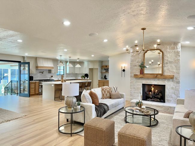 Living room featuring a textured ceiling, light wood finished floors, a chandelier, recessed lighting, and a fireplace | Image 4