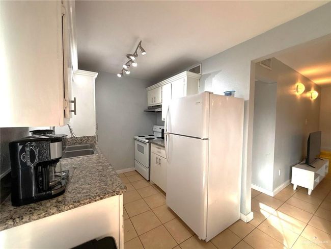 Kitchen with visible vents, white appliances, light tile patterned flooring, and under cabinet range hood | Image 8