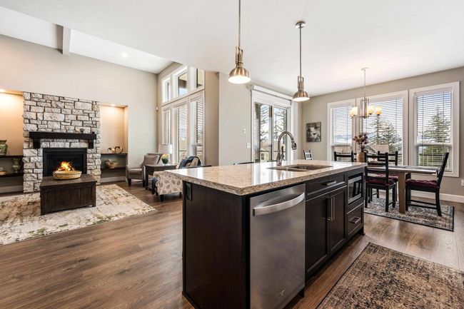 Kitchen with light stone counters, a sink, a stone fireplace, stainless steel appliances, and dark wood-type flooring | Image 17