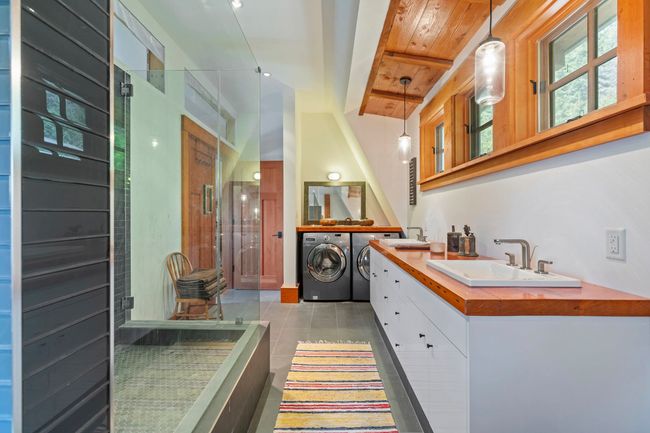 Full bath with washer and clothes dryer, double vanity, a shower stall, tile patterned flooring, and wood ceiling with exposed beams | Image 22
