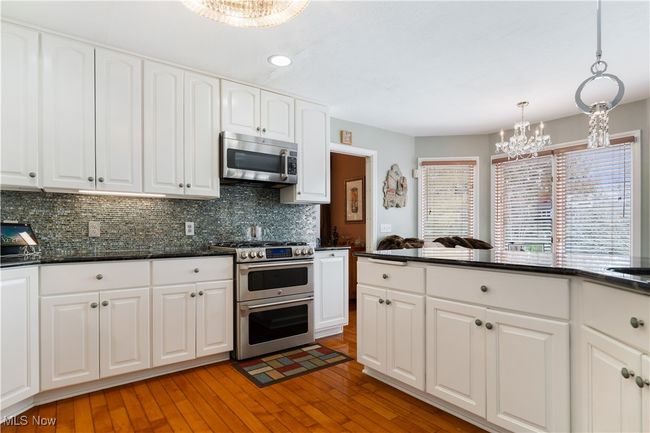 Partial view of the kitchen with light wood-style floors, appliances with stainless steel finishes, decorative light fixtures, backsplash, and a chandelier | Image 10