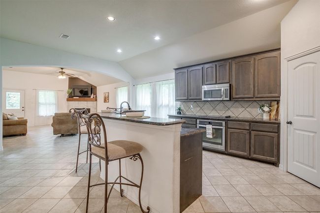 Kitchen featuring appliances with stainless steel finishes, a breakfast bar, lofted ceiling, backsplash, and open floor plan | Image 11